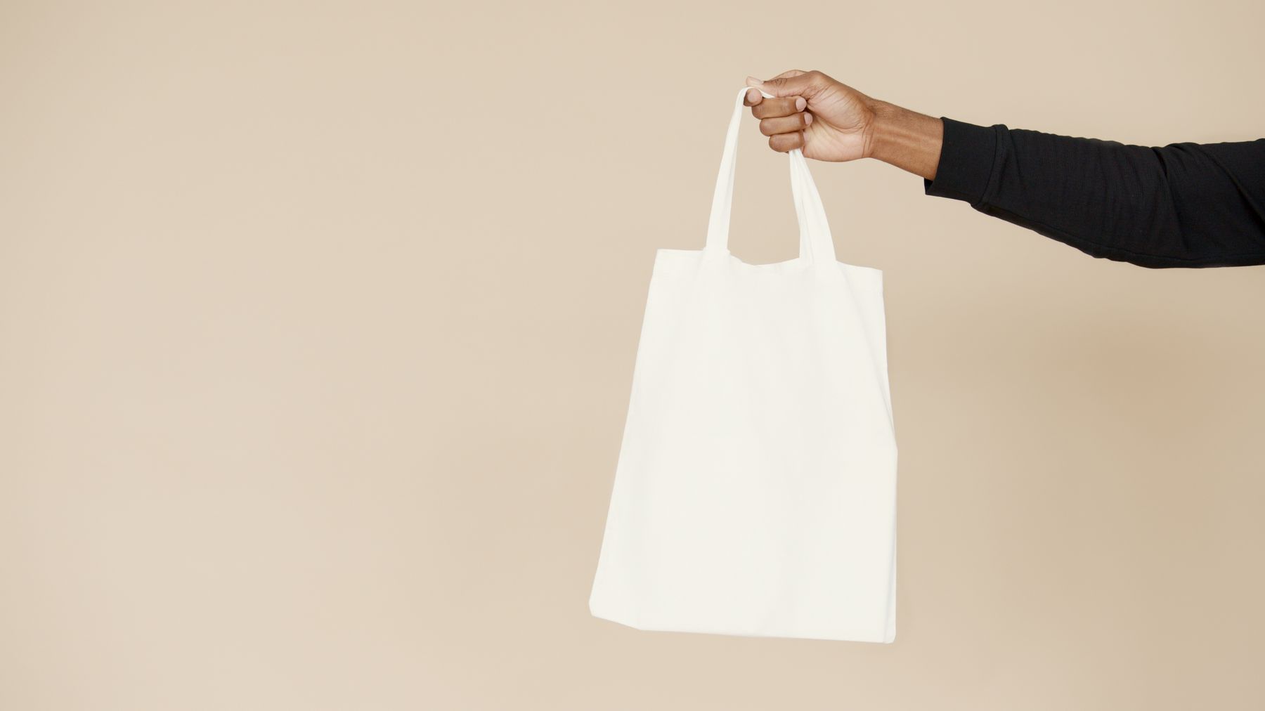 A real white tote bag held against a warm beige studio background.